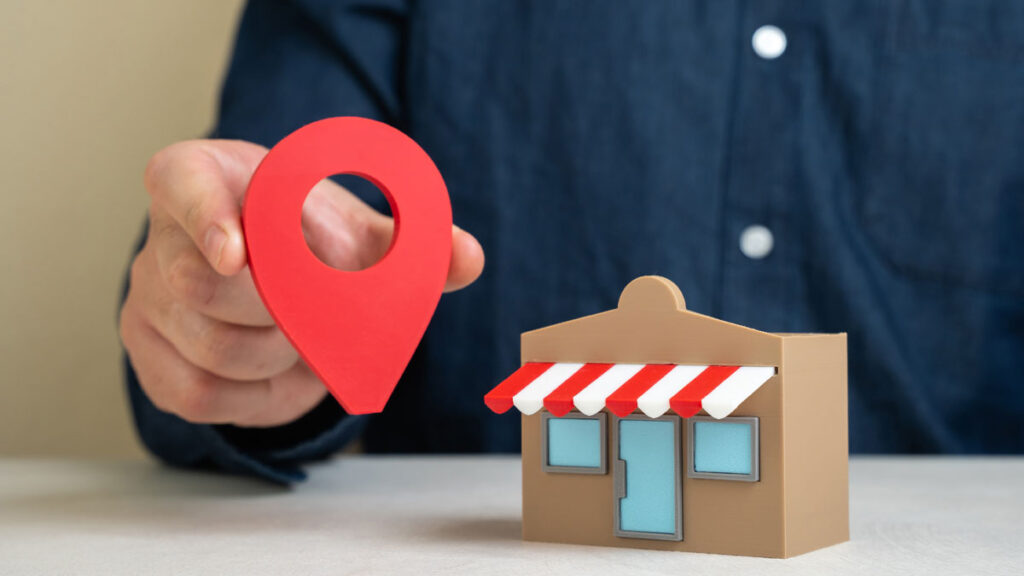 A man holds a geolocation pin near a store. Local SEO increases business visibility. 